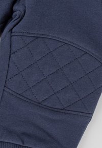 Navyblaue Sweatshirt-Stoff mit einem gesteppten Rautenmuster im Ellenbogenbereich, gerippten Bündchen und glatter Textur.
