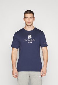 Granatowa bawełniana koszulka z krótkim rękawem, z logo "New York Yankees" i metką Champion na rękawie dla podkreślenia marki.
