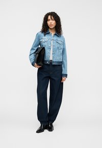 Φωτεινό γαλάζιο τζιν μπουφάν με θήκες με καπάκι και γιακά, συνδυασμένο με χαλαρά σκούρα μπλε τζιν. Το μοντέλο κρατάει ένα μαύρο clutch. Μαύρα παπούτσια.