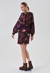 Kurzes lila- und braunblumiges Kleid mit Puffärmeln und gerafften Bündchen, kombiniert mit braunen Wildleder-Stiefeletten mit seitlichem Reißverschluss.