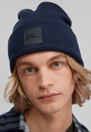 Donkerblauwe ribgebreide beanie met een opgerolde rand en een zwart vierkant logo-patch. Zachte stof met een snug, aansluitende pasvorm.