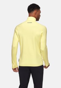Lichtgele langlopende shirt met hoge kraag, met een zwart logo op de achterkant, een gladde textuur en contrasterende naden.
