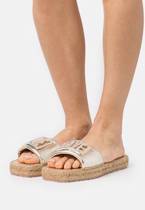 Złote metaliczne klapki na płaskim obcasie z plecioną podeszwą z juty, ozdobione paskiem z kryształkami układającym się w napis "LOVE" wykonany ze złotych i przezroczystych cyrkonii.