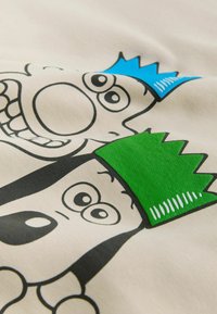 Baumwoll-T-Shirt mit Cartoon-Figuren, die blaue und grüne Kronen auf einem hellen cremefarbenen Hintergrund tragen, schwarz umrandet, glatte Textur.