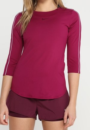 Maroon urheilu paita, jossa on kolme neljännestä hihat, valkoiset sivusuunnat ja pieni musta logo. Yhdistetty vastaavansävyisiin maroon shortsseihin.