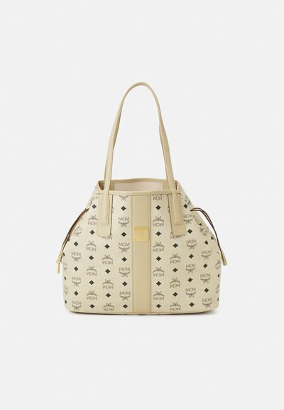 Sac seau beige en cuir, arborant un motif logo répété, avec deux poignées supérieures et des accents en métal doré. Poche latérale zippée.