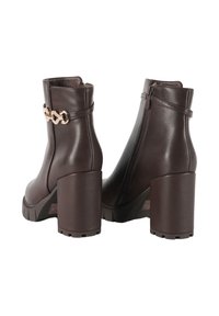 Stivaletti alla caviglia in finta pelle marrone con tacco a blocco spesso, cerniera laterale e un accentuato dettaglio in catena dorata. Suola in gomma per una migliore aderenza.