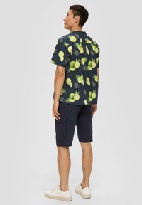 Korte mouwen, marineblauw shirt met een limoenen en bladerenpatroon, gemaakt van katoen, gecombineerd met donkere shorts en witte sneakers.