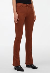 Jean marron ajusté avec une coupe évasée, fabriqué en denim. Associé à des bottes noires à talons pointus. Ceinture simple avec poches avant.