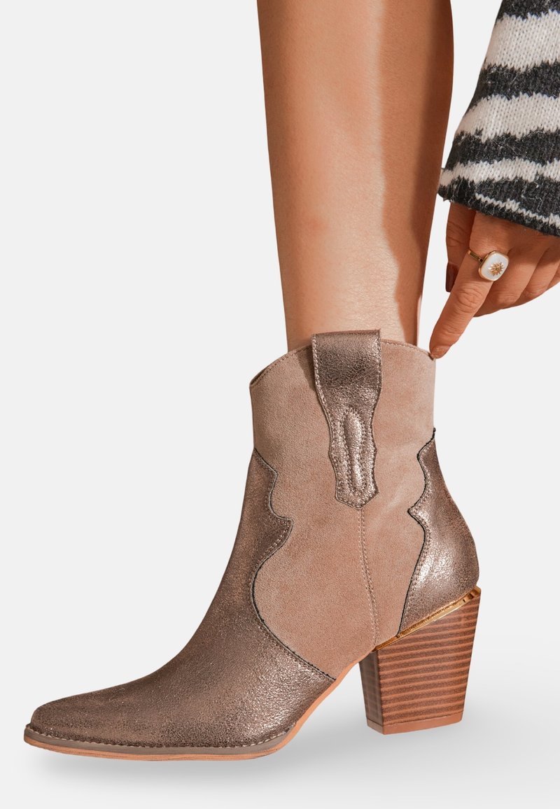Bottes chelsea en daim marron avec une finition métallisée, bout pointu et couture décorative. Présente un talon empilé avec des rainures horizontales.