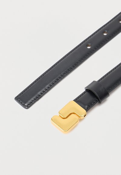 Μαύρη δερμάτινη ζώνη με μοναδική χρυσή αγκράφα που διαθέτει δύο αλληλοσυνδεόμενα γεωμετρικά σχήματα σε ανοιχτό φόντο.