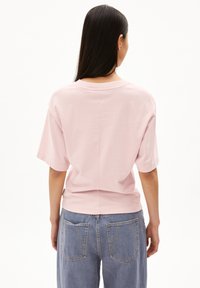 Helles rosa Kurzarm-T-Shirt mit Rundhalsausschnitt und lockerem Schnitt; weicher Baumwollstoff; kombiniert mit hoch-taillierten blauen Jeans.