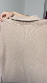 Beige, ribbed knit sweater with a wide neckline and relaxed fit, featuring a textured surface and soft fabric. No visible hardware or patterns.
