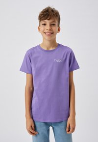 T-shirt en coton violet à manches courtes et encolure ras du cou, portant l'inscription blanche "T.W.S.N." sur la poitrine gauche. Coupe décontractée.