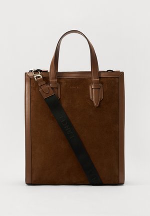 Braune Wildleder- und Leder-Tote-Tasche mit zwei oberen Griffen und einem verstellbaren Riemen, der ein schwarzes Logo auf dem Riemen und eine glatte Oberfläche aufweist.