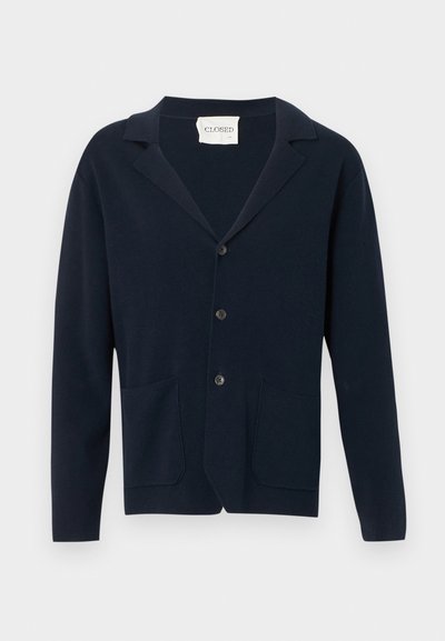 Gilet boutonné bleu marine avec deux poches à l'avant et un col, présenté sur un fond blanc.