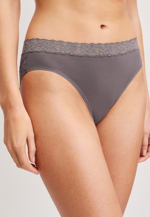 Vrouw draagt grijze onderkleding met een kanten tailleband en zijkantdetails, staand tegen een effen lichte achtergrond.
