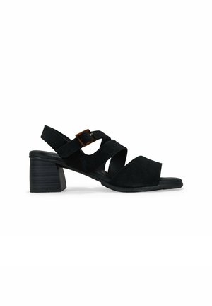 Sandalias de tacón de ante negro con correas cruzadas y un acento de hebilla. Tacón bajo y diseño de punta abierta. Textura suave, silueta minimalista.