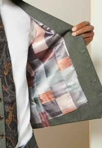 Chaqueta de traje gris con un forro interior de satén a rayas multicolores, que presenta tonos de azul, melocotón y gris, y una corbata con estampado.