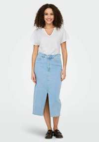 Jasnoniebieska spódnica dżinsowa z rozcięciem z przodu, wysoki stan, dopasowany krój, zestawiona z białym T-shirtem z dekoltem w serek i czarnymi butami typu slip-on.