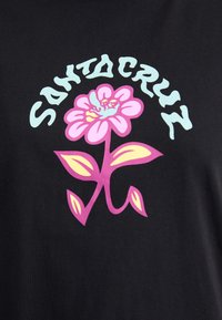 Juodas marškinėliai su didele rožine gėlės grafika, accentuota žalia spalva, ir užrašu "SANTA CRUZ" šviesiai mėlynos spalvos virš gėlės dizaino.