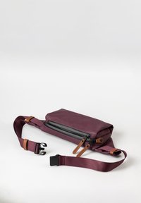 Borsa a spalla bordeaux con superficie liscia, tasca con zip nera, tracolla regolabile e dettagli in pelle. Forma rettangolare compatta.