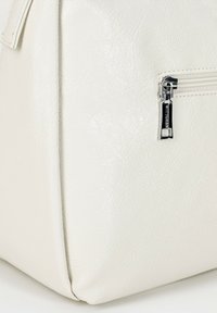 Torebka wykonana z białej sztucznej skóry o teksturowanym wykończeniu, z metalowym suwakiem po boku. Projekt ma kątowy kształt, z wyraźnie zarysowanymi bokami i gładką powierzchnią.