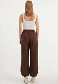 Braune weite Hosen mit elastischem Bund, kombiniert mit einem taillierten weißen Rippen-Crop-Top. Weiche Textur und lockere Passform.
