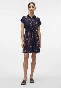 Vestido floral azul-marinho com mangas curtas, colarinho e cinto. Apresenta padrões florais em rosa, tecido leve e saia rodada. Sandálias de slide pretas.