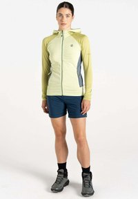 Helles grünes Zip-Hoodie mit einem strukturierten Muster, grauen Akzenten, langen Ärmeln, kombiniert mit marineblauen Shorts und grauen Wanderschuhen.