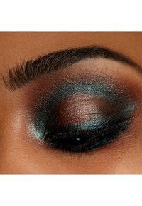 Gros plan sur un œil avec un maquillage élaboré comprenant des fards à paupières teal et marron scintillants, des cils bien définis et des sourcils soigneusement entretenus.