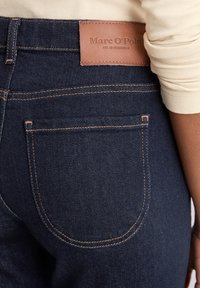 Donkerblauwe denim jeans met zichtbare oranje stiksels, leren merklabel op de tailleband en standaard ontwerp van de achterzak. Gestructureerde stof.