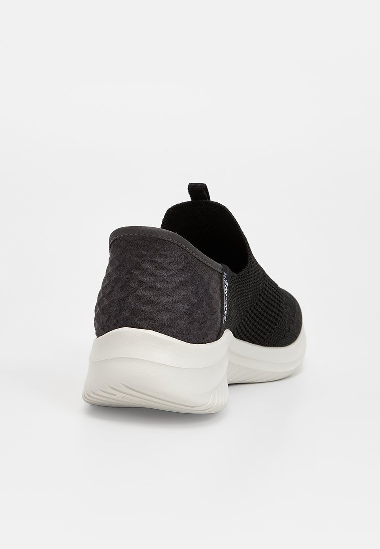 Svart slip-on sneakers med texturerad tygövre och en slät vit sula, utrustad med en dragflik för enkel påtagning och en minimalistisk design.