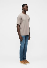 Gray cotton t-shirt with a chest pocket, paired with blue jeans and tan sneakers. Simple, straight-cut design, and light texture.