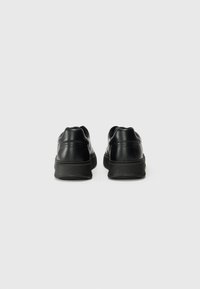 Baskets en cuir noir avec une texture lisse, bout arrondi et semelle rembourrée. Présentent un talon proéminent et un design minimaliste.