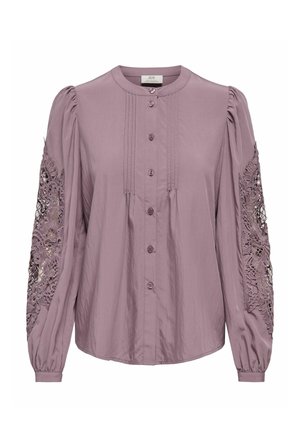 Blouse lilas avec un col rond, une patte de boutonnage à l'avant et des manches longues bouffantes ornées de détails en dentelle délicate sur les bras. Tissu léger.