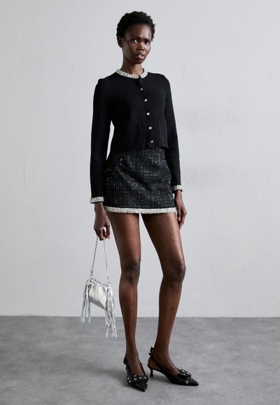 Crni kratki kardigan s srebrnim gumbima, uparen s mini suknjom od tvida s sjajnim rubom, ukrašen srebrnom torbom s resicama.