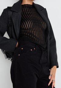 Top negro transparente de manga larga con rayas horizontales, combinado con un blazer gris oscuro y pantalones negros de tiro alto con botones de cobre.