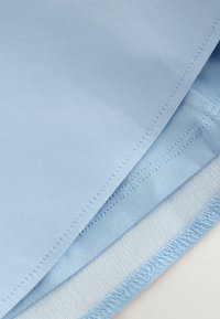 Gaiši zilas auduma kārtas ar redzamām šuvēm un salocītām malām, parādot tekstūru un šuves uz gludas tekstila virsmas.