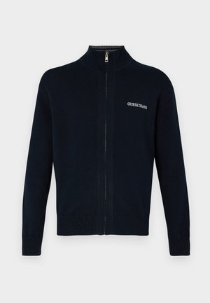 Navy zip-up cardigan made of ribbed knit fabric, featuring a high collar, long sleeves, and a subtle logo on the left chest.