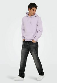 Gaiši violets džemperis ar kapuci, priekšējā kabata, aukliņām un melnām detaļām; kombinēts ar tumši pelēniem džinsiem un baltām kurpēm.