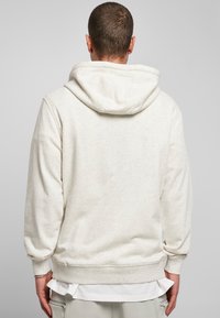 Felpa con cappuccio grigia chiara in fleece, dotata di cappuccio con coulisse, polsini e orlo a costine. Presenta una texture liscia e una cucitura minimale.