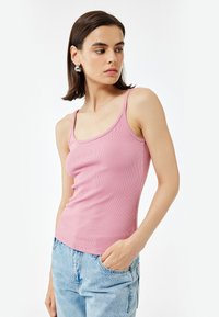 Roze geribbelde tanktop met brede bandjes, aansluitend ontwerp en een gebogen halslijn. Gepaard met lichtblauwe denim jeans.