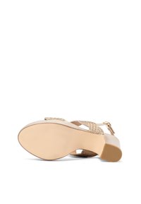 Sandal con tacco beige con parte superiore texture, design a tracolla incrociata e fibbia regolabile. Suola liscia con punta leggermente arrotondata.