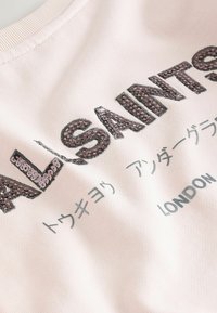 Ljust rosa tyg med paljetter och texten "LASTING" samt tryckt mindre text på japanska och "LONDON" i grått.