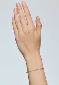 Srebrna bransoletka na nadgarstku, z małymi okrągłymi i owalnymi koralikami, prezentująca delikatny wzór i gładką strukturę.