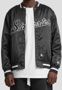 Veste bomber en satin noir avec inscription "Starter", accents blancs, boutons-pression et poignets ainsi que ourlet côtelés rayés. Comprend un patch logo en détail.