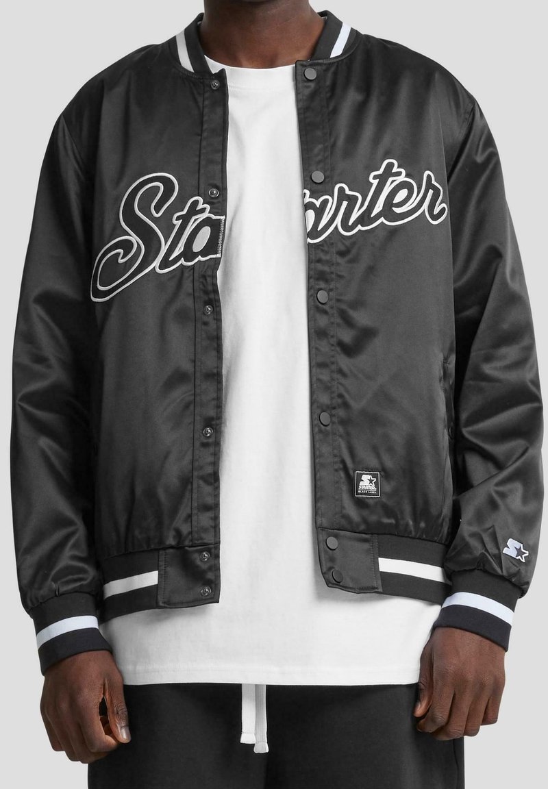 Veste bomber en satin noir avec inscription "Starter", accents blancs, boutons-pression et poignets ainsi que ourlet côtelés rayés. Comprend un patch logo en détail.