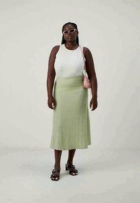 White sleeveless top and green ribbed midi skirt. Accessorized with pink bag and black sandals. Minimalist design with smooth textures.