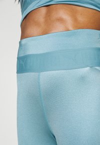 Leggings de sport bleu clair avec une large taille en relief. Le tissu a une surface brillante et texturée avec des détails de couture visibles.